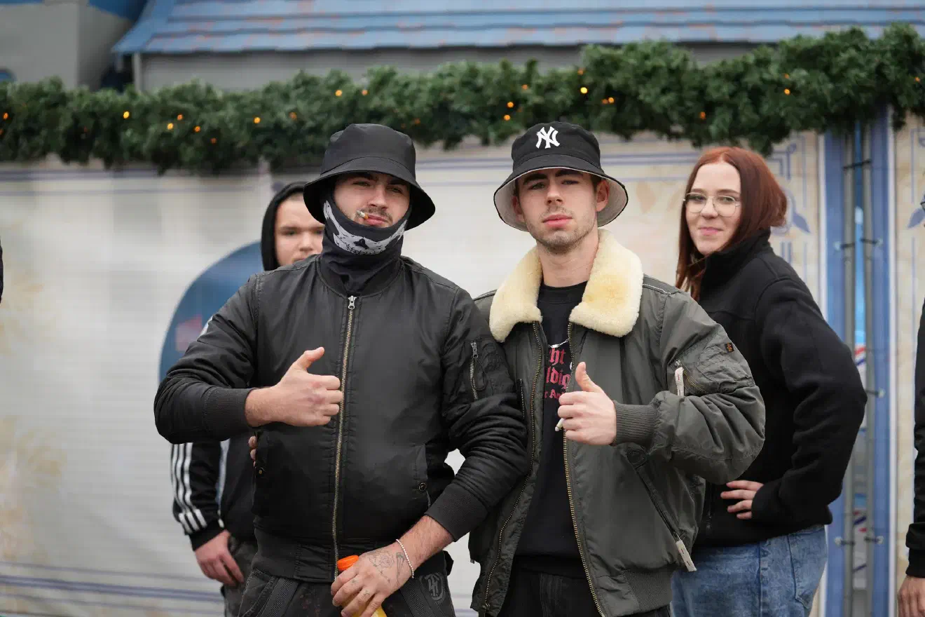Der Handgruß mit abgeknicktem Daumen, der sogenannte "Tessak-Gruß", bezieht sich auf einen russischen Neonazi, der besonders durch besonderen Rassismus und Hass auf Homosexuelle bekannt ist. Er ist für grausame Taten an homosexuellen Männern verantwortlich, die unter dem Deckmantel der "Jagd auf Pädophile" begangen wurden.